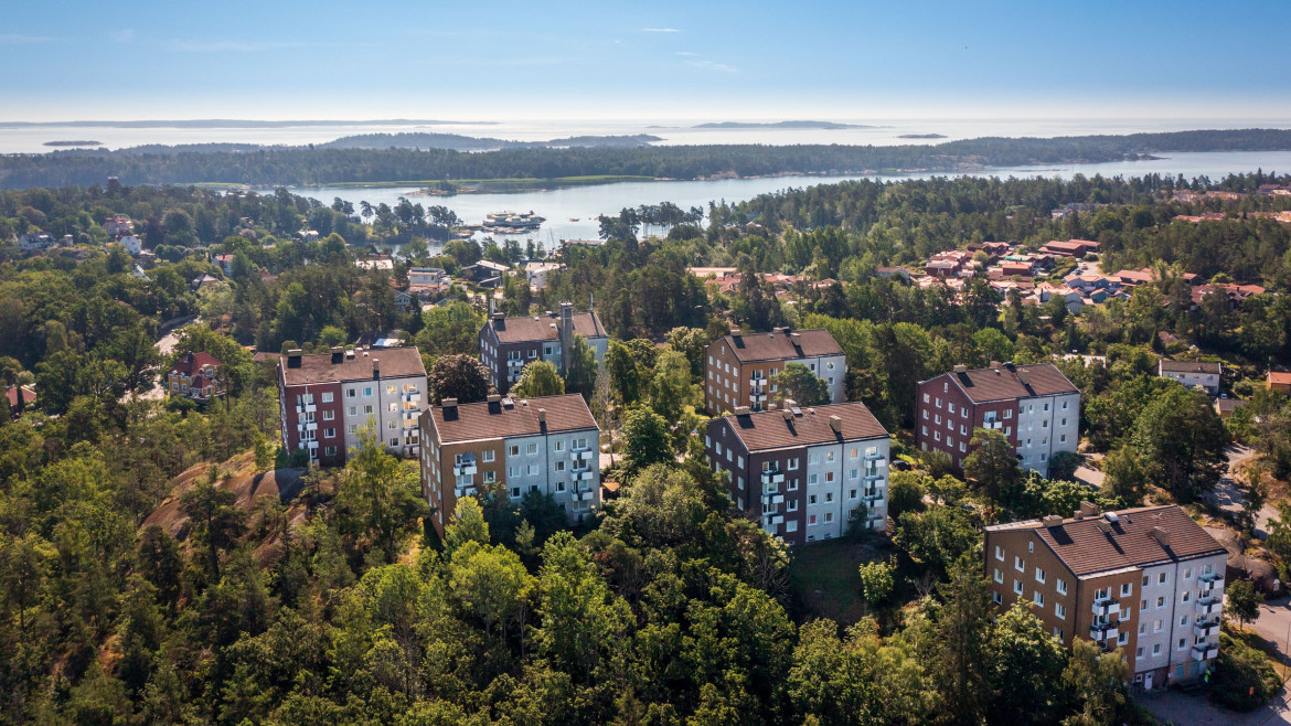 Flera flerfamiljshus omgivna av frodig grönska längs Toppstigen i Nynäshamn. I bakgrunden syns skärgården med vatten och små öar som sträcker sig mot horisonten.