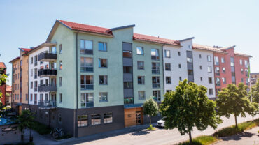 Flerfamiljshus på Lövlundsvägen 8 A till C i Nynäshamn. Byggnaderna har olika fasadfärger och är utrustade med balkonger. Träd och trottoar pryder framsidan av gatan, vilket skapar en inbjudande atmosfär i bostadsområdet.