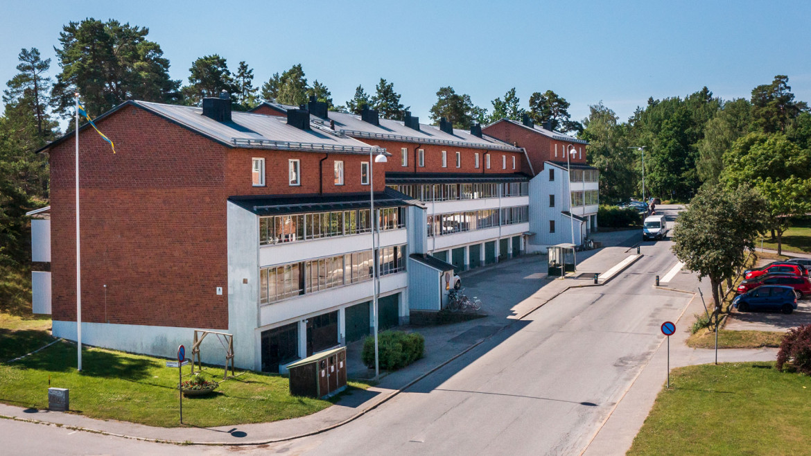 Hyreslägenheter på Estövägen 5 A och B i Nynäshamn, med röda tegelbyggnader och balkonger, omgivna av träd och grönska. Perfekta hyreslägenheter i en naturskön miljö.