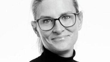 Porträtt av Annika Kurtsson, VD för Nynäshamnsbostäder, iförd glasögon och en mörk tröja med hög krage.